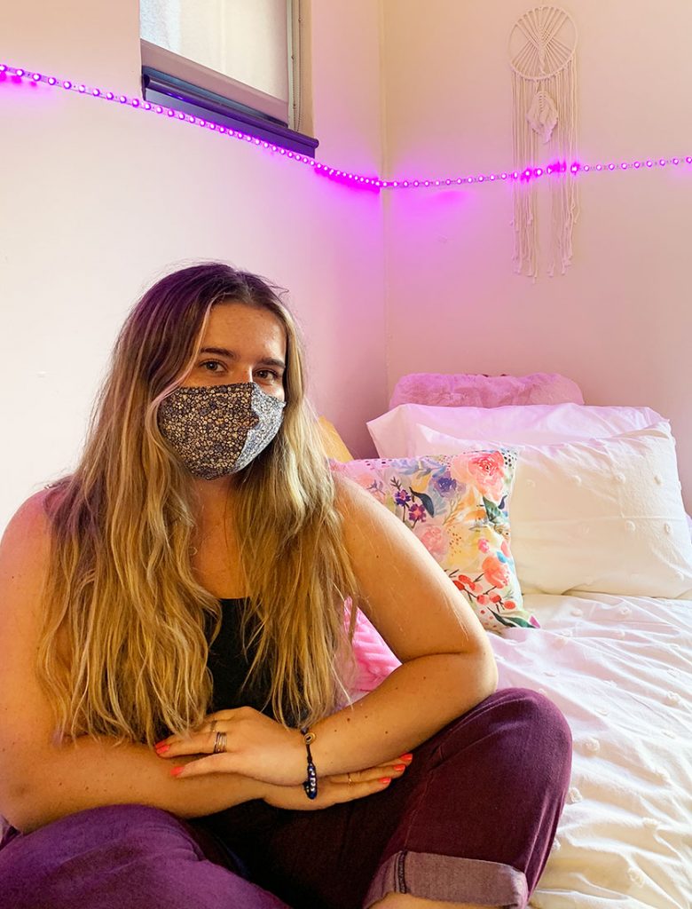emma sitting on bed with floral face mask