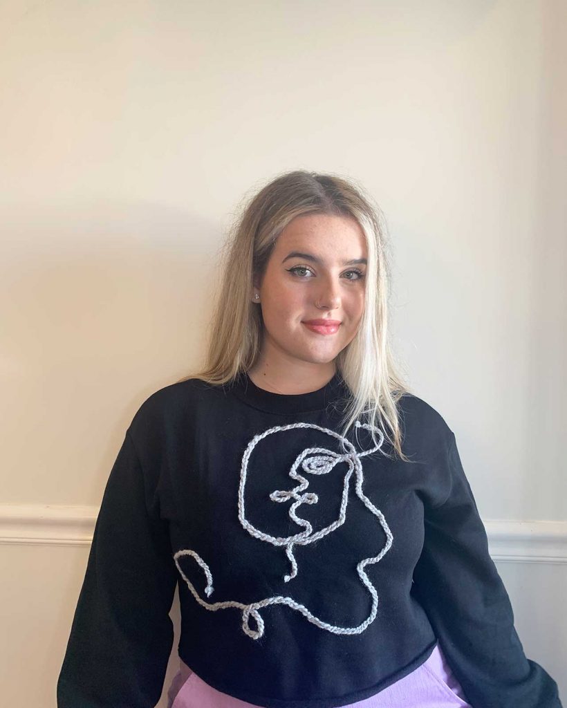 girl in black sweatshirt with grey yarn art in shape of a face