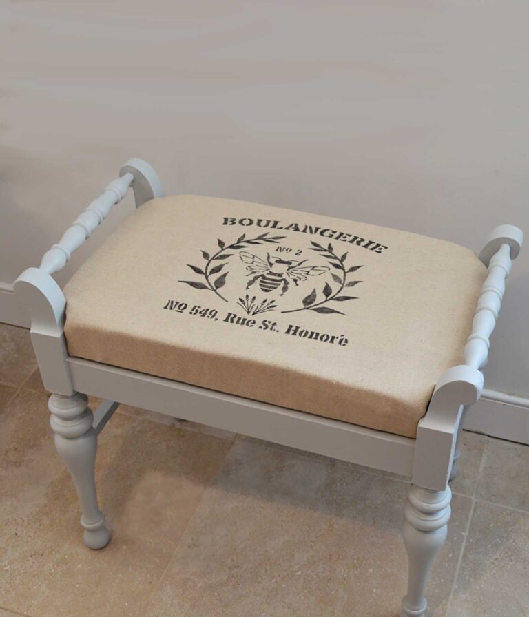 upholstered painted grey bench with stencil on cushion that reads Boulangerie no 549 rue st. Honoré with a bee and leaf graphic in center