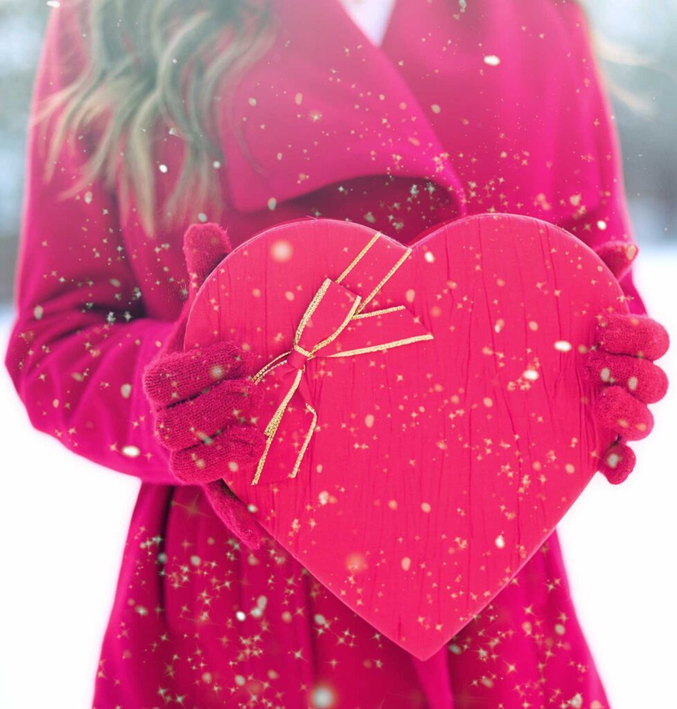 woman in red coat and gloves holding a red heart box of valentines day candy with a bow