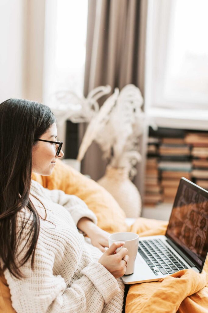 Woman sitting on couch with laptop in cozy athflow clothes 