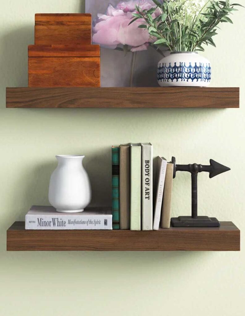two wood floating shelves with stacked boxes, plant, art, lower shelf with books, vase and metal arrow.