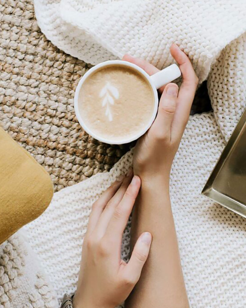 Self care during the holidays. Woman's hands holding a cup of coffee  over a blanket.