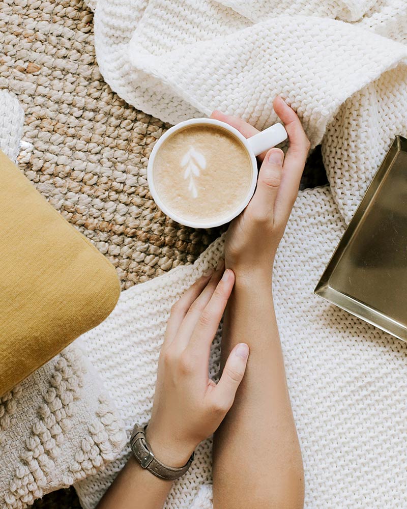 woman hands holding a cup of coffee on top of blankets