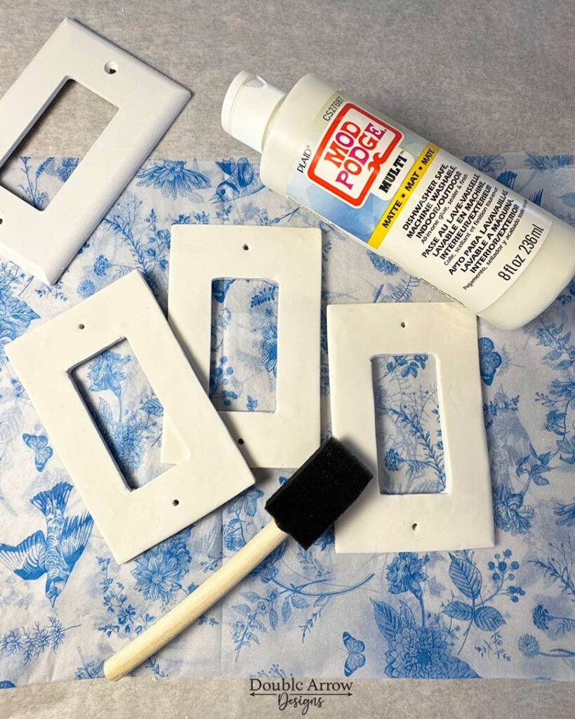 unfinished polymer clay light covers on top of blue ad white toile printed paper with mod podge and foam brush